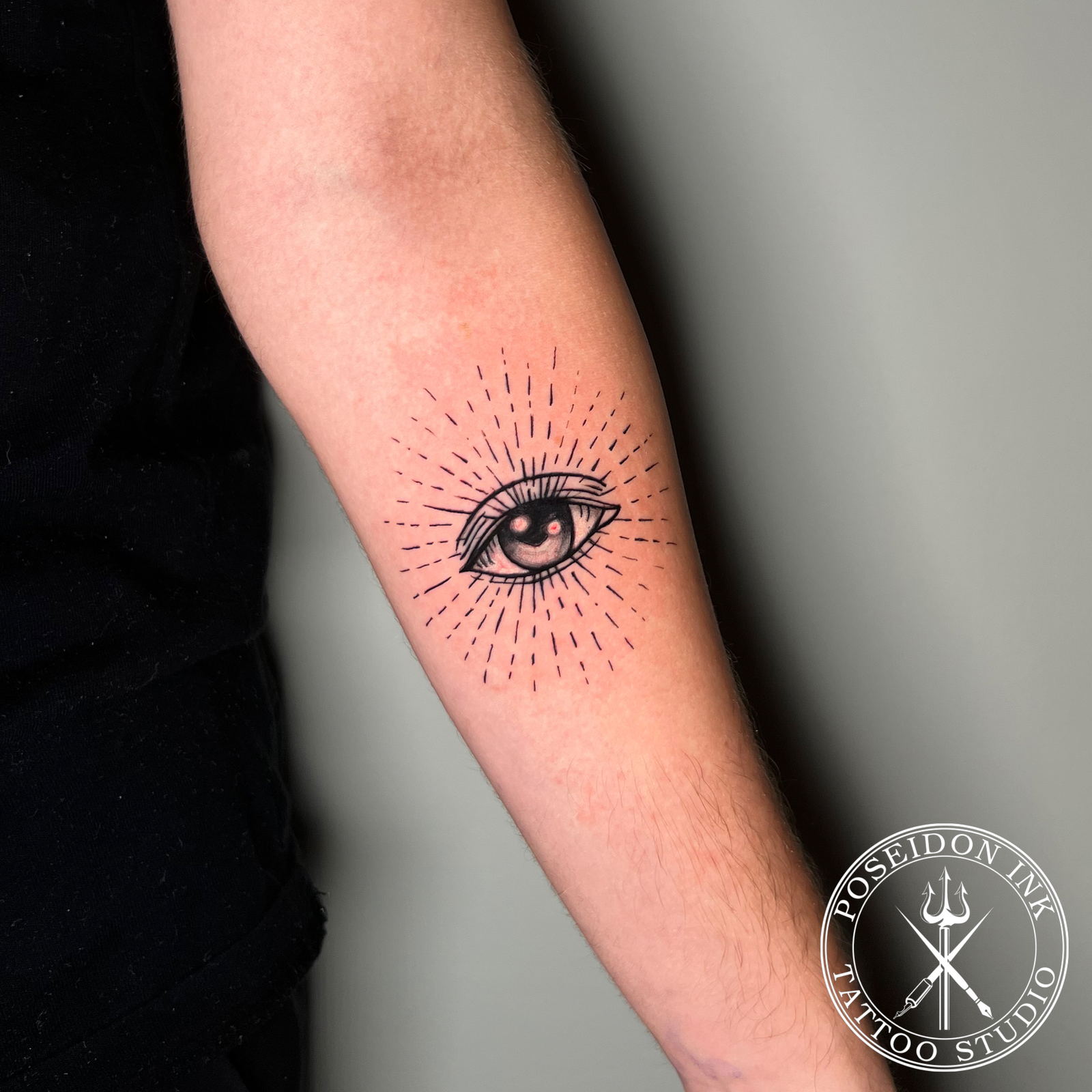 Illustrative tattoo of a single eye at the centre of radiating dashed sunburst rays on the forearm