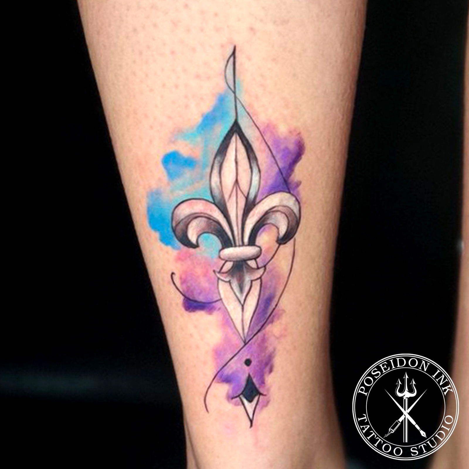 Tattoo of a shaded fleur-de-lis emblem over blue, purple and pink watercolour splashes on the lower leg