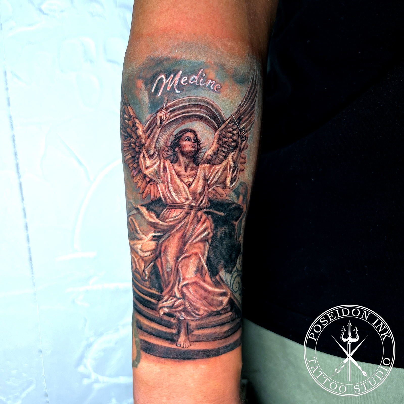 Colour realism tattoo of a winged angel standing on stone steps with the name Medine in white ink script above