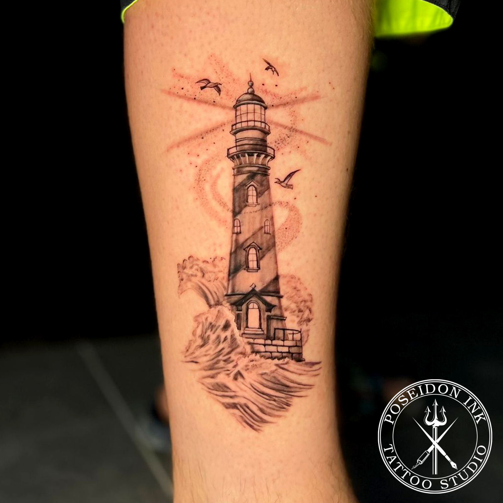 Black and grey realism tattoo of a spiral striped lighthouse on rocks with crashing waves and seagulls, on the calf