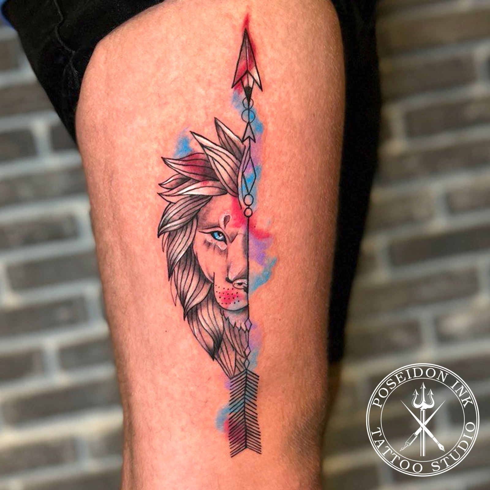 Illustrative tattoo of half a lion face mirrored on a vertical arrow with blue and purple watercolour splashes, on the thigh