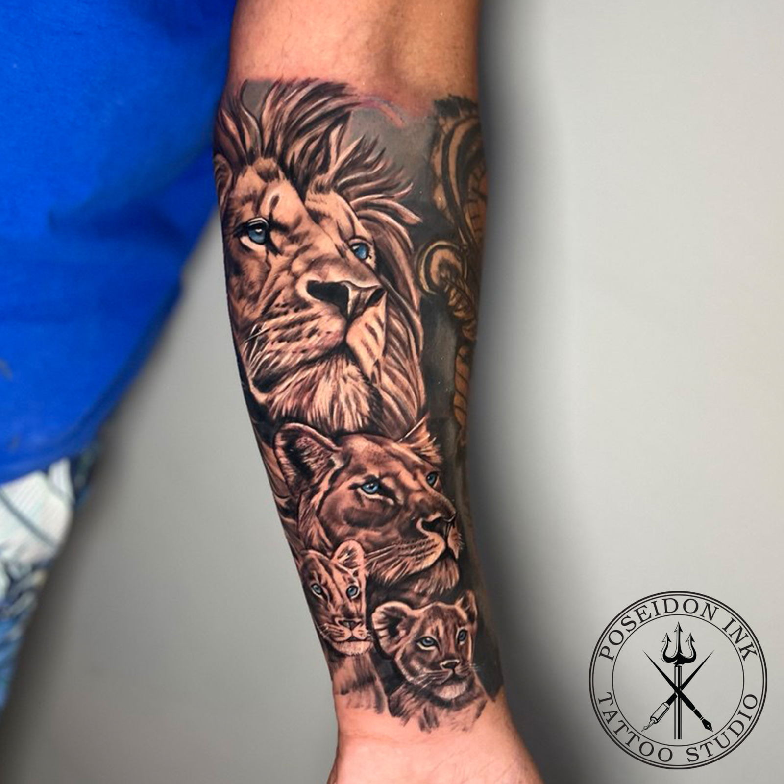 Black and grey realism tattoo of a lion, lioness and two cubs with pale blue eyes stacked down the forearm