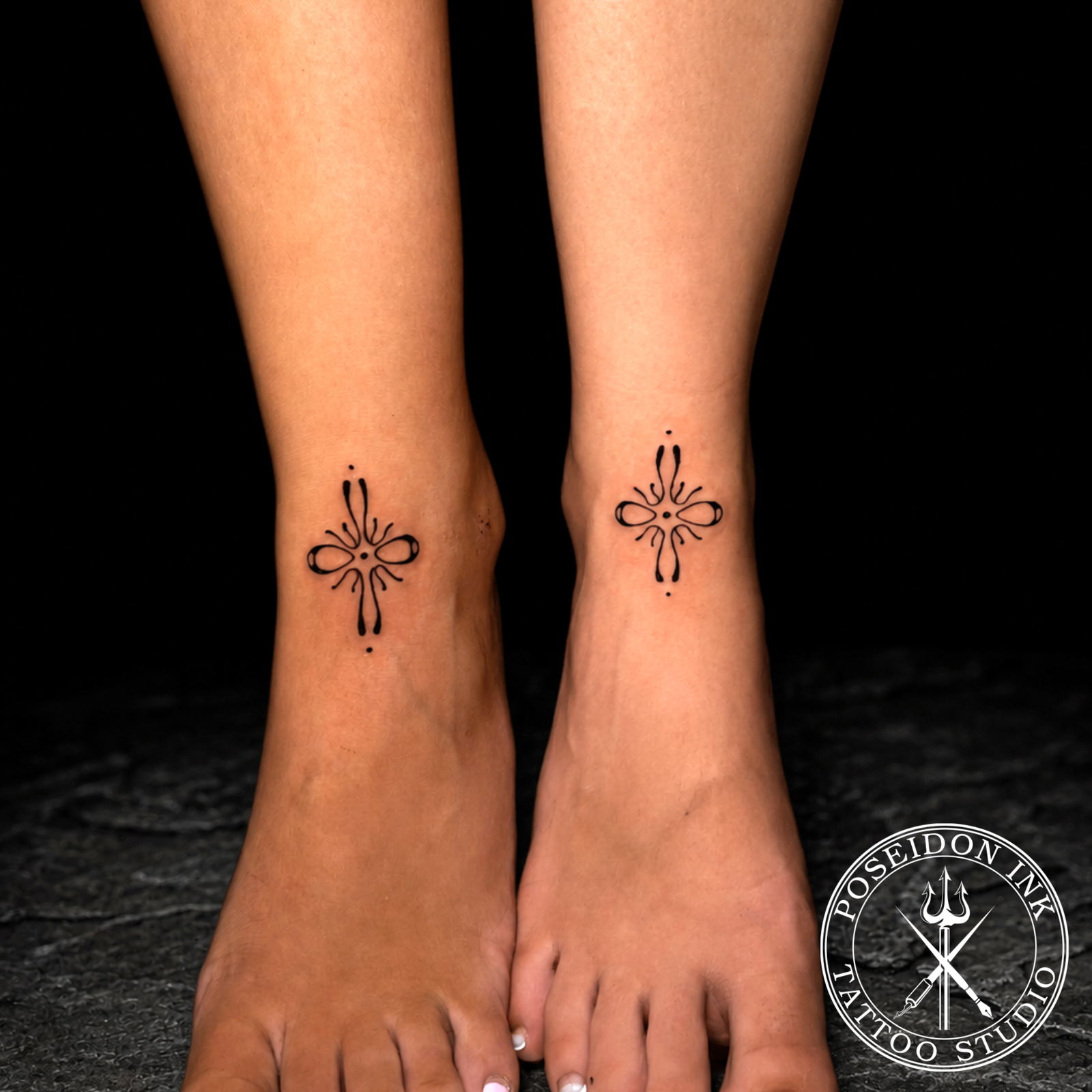 Matching minimalist ornamental tattoos drawn in fluid droplet style strokes on two ankles