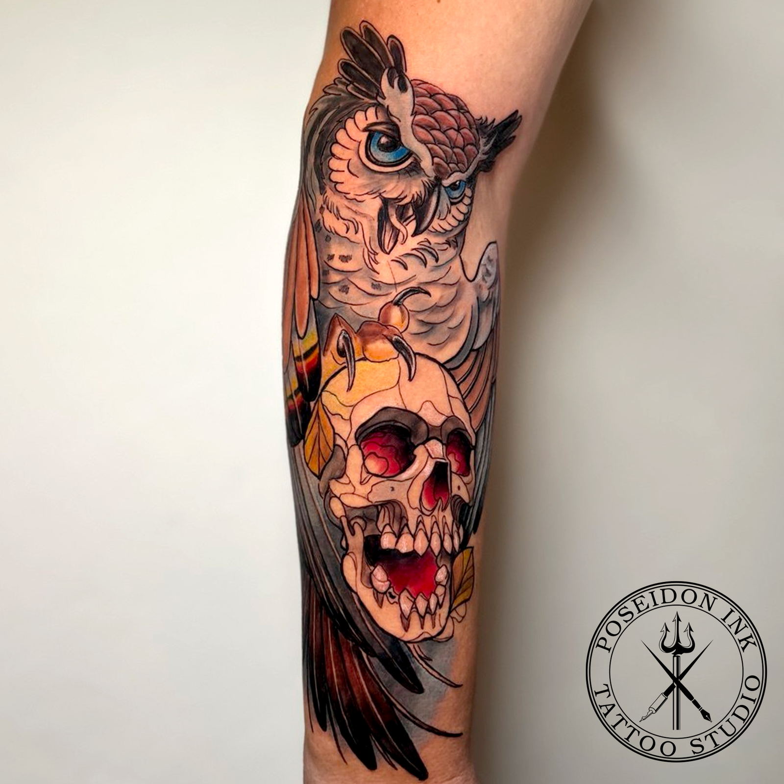 Neo-traditional colour tattoo of an owl with blue eyes perched on a red-eyed skull, forearm piece