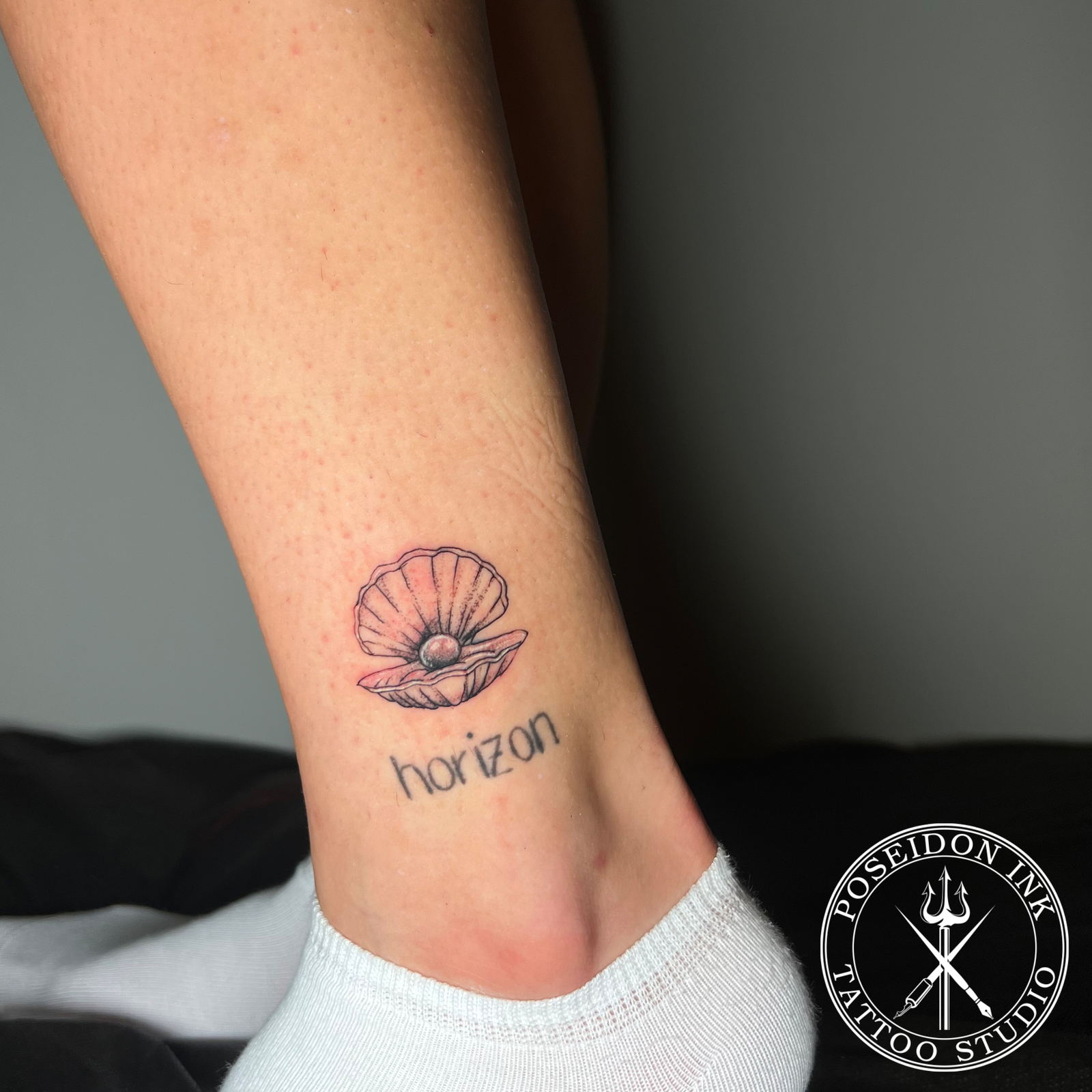 Fine line tattoo of an open oyster shell holding a pearl, with stippled dot shading, above the ankle