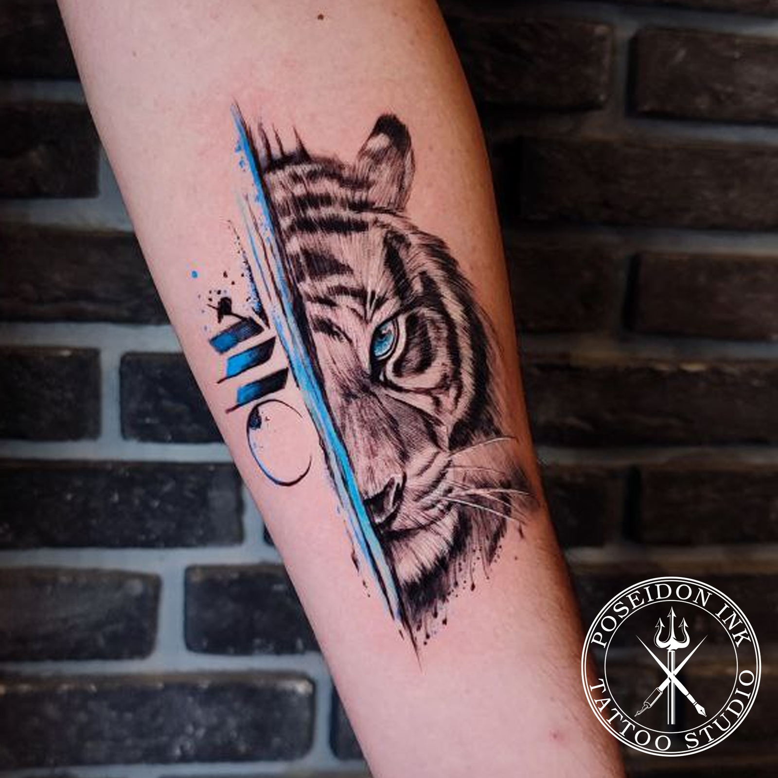 Black and grey tiger face tattoo with vivid blue eye, sliced by abstract blue brushstroke stripes on the forearm