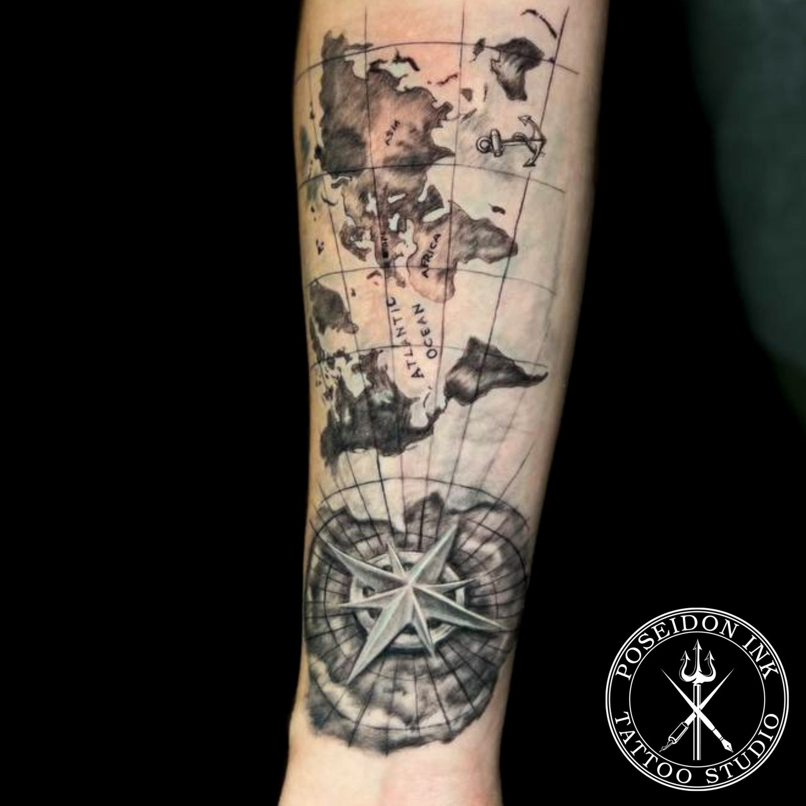 Black and grey tattoo of an antique world map with anchor and birds, converging into a nautical compass star at the wrist