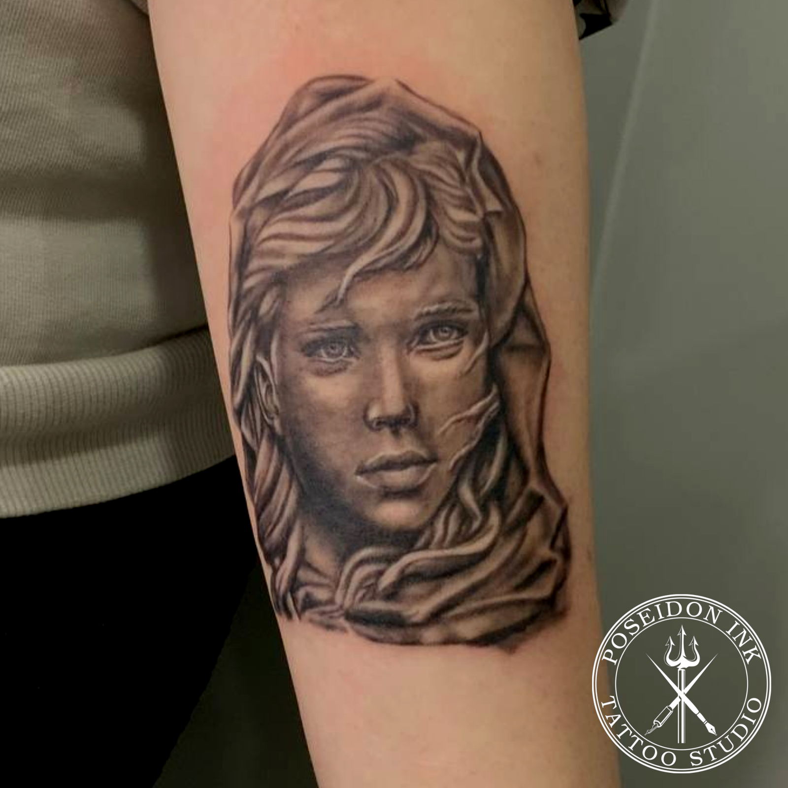 Black and grey realism tattoo portrait of a woman with flowing hair and a draped veil, on the upper arm